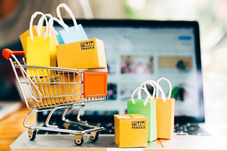 Miniaturní nákupní vozík s barevnými taškami a krabicemi před notebookem s e-shopem, ilustrace SEO pro e-shopy.