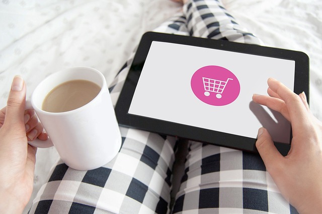 Osoba s hrnkem kávy nakupuje na tabletu se symbolem růžového nákupního košíku, ilustrace pohodlného online nákupu v e-shopu